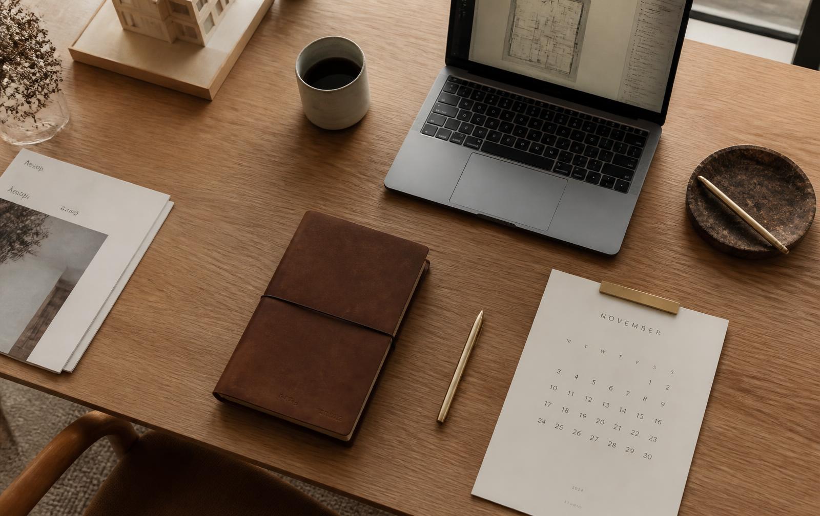 Designer's desk with notebook, laptop, coffee and a calendar